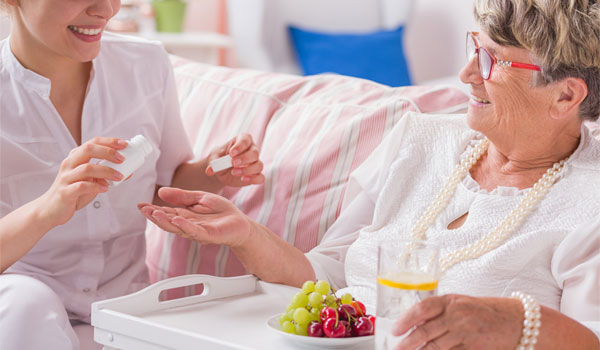 Alltagsassistentin verabreicht einer Seniorin ihre Tabletten