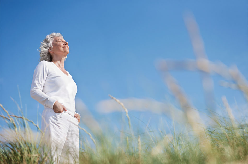 Eine ältere Frau steht auf einer Düne und genießt den Urlaub von der Pflege.