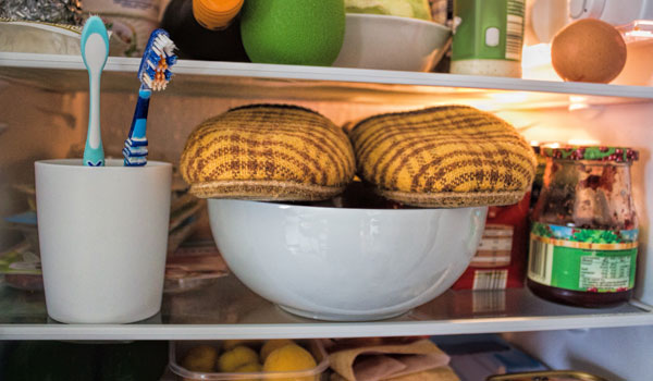 Ein Kühlschrank in dem Pantoffeln und ein Zahnputzbecher mit zwei Zahnbürsten liegen.