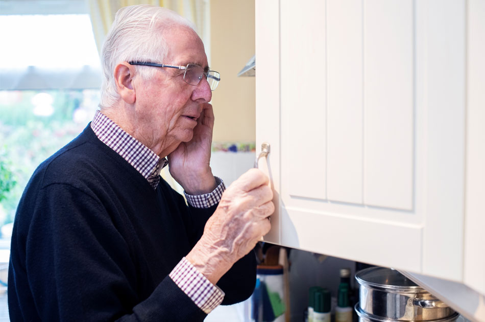 Ein Demenzkranker Mann schaut in seinen Küchenschrank und weiß nicht mehr was er gerade tun wollte.