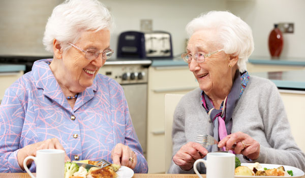 Zwei Seniorinnen unterhalten sich beim Essen in der Küche.
