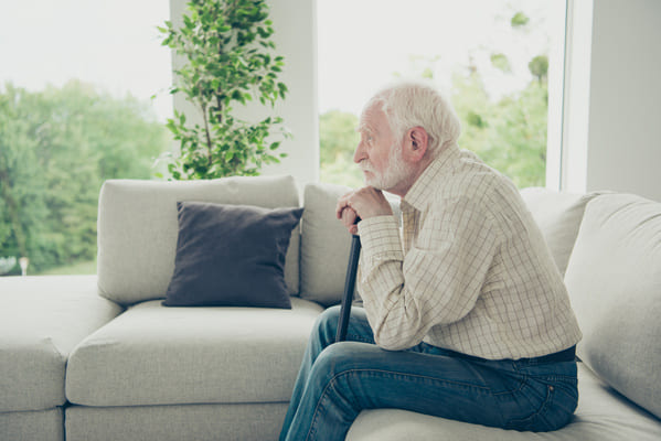 Ein Senior sitzt depressiv und lustlos auf der Couch im Wohnzimmer.