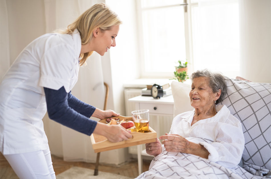 Unterstützungspflege: Eine ältere Dame bekommt das Bett von einer Alltagsassistentin ans Bett gebracht.