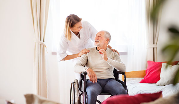 Verhinderungspflegerin unterhält sich mit einem Senior, der im Rollstuhl sitzt.