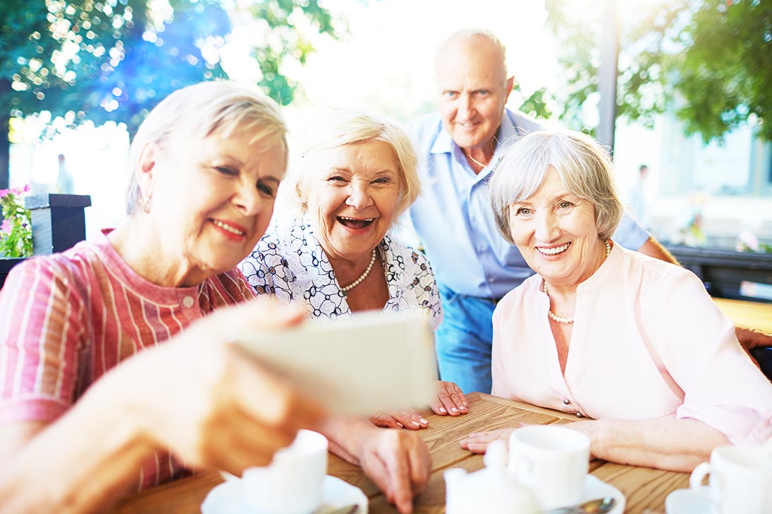 Eine Seniorengruppe aus drei Frauen und einem Mann schauen auf ein Handy.