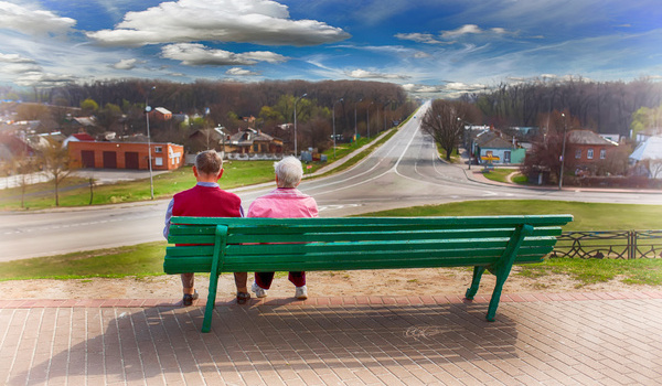 Ein Seniorenpaar auf einer Parkbank blickt auf ein Demenzdorf.