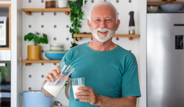 Ein älterer Mann trinkt ein Glas Milch, um keinen Eiweißmangel zu erleiden.