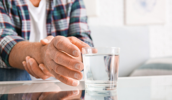 Ein Senior, welcher an Parkinson erkrankt ist, greift nach einem Wasserglas und hält dabei seinen Greifarm fest.