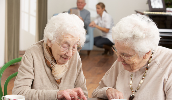 Zwei Seniorinnen spielen in einer Tagespflege-Einrichtung Domino.