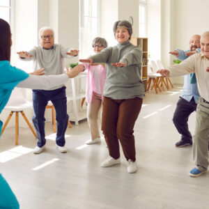 Eine Physiotherapeutin zeigt einer Seniorengruppe eine Gymnastikübung.
